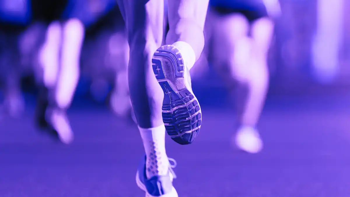 Close-up of a marathon runner’s shoe mid-stride with blurred runners behind, highlighting movement driven by repetition and focus rather than visible surroundings