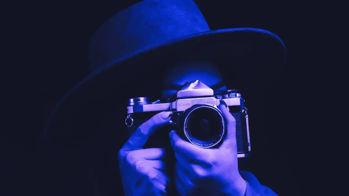 Blue-toned close-up of a photographer holding a camera, representing image sourcing, visual licensing, and editorial content control.