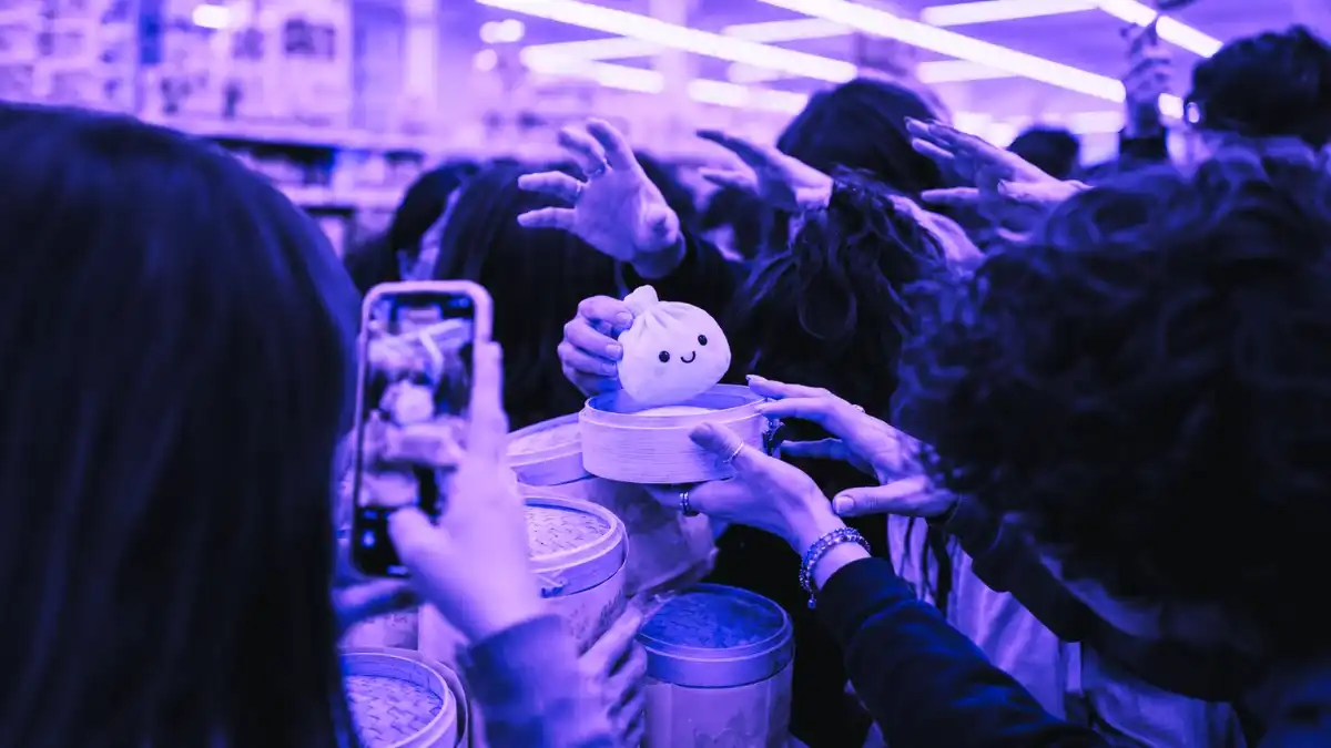 Shoppers reaching for a cute dumpling plush toy in a bamboo steamer during a crowded viral toy drop, showing the excitement and urgency around the Five Below Dumpling Drop.
